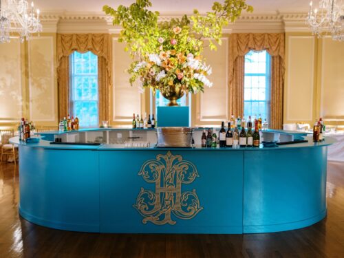 customizable oval bar painted teal with a custom decal crest on the front with the customizable pedestal inside the bar to hold a floral arrangement inside farmington country club for an indoor wedding